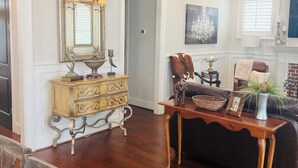 A spacious living room with hardwood flooring, a dark leather sofa, a wooden coffee table, and a decorative mirror. - 3-Bed, 3.5-Bath Home Just 4.8 Miles from Golf Course in a Stunning Neighborhood! (Evans)