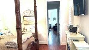 A bedroom with a four-poster bed, a television mounted on the wall, and a hallway leading to another room. - 3-Bed, 3.5-Bath Home Just 4.8 Miles from Golf Course in a Stunning Neighborhood! (Evans)