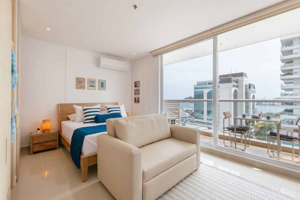 A bedroom with a bed, bedside table, and a view of the city.