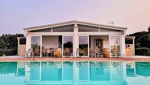 Una casa moderna con piscina, que cuenta con un porche cubierto y mobiliario exterior.