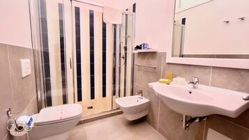 A bathroom with a toilet, bidet, sink, and a glass shower enclosure.