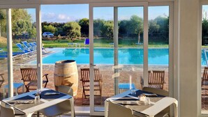 Zona de comedor junto a la piscina con mesas y sillas, vista a una alberca y cielo despejado.