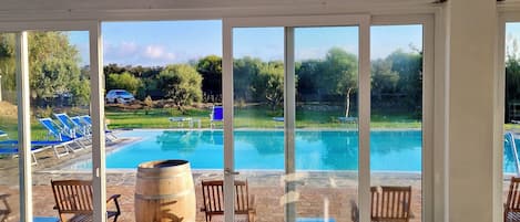 Zona de comedor junto a la piscina con mesas y sillas, vista a una alberca y cielo despejado.