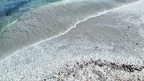 Una playa con agua cristalina, un bote y gente a lo lejos.
