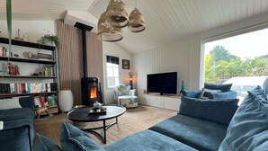 A modern living room with a large sofa, a bookshelf, a fireplace, and a television. - Charming villa - Swimming pool - Spa - Pond (Saint-Hilaire-de-Riez)