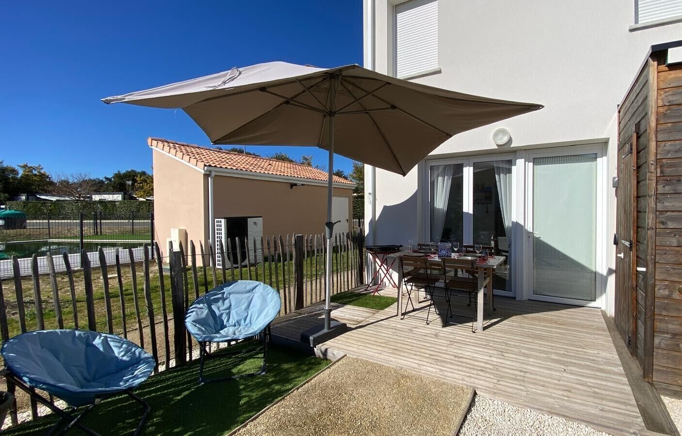 Un pati amb taula i cadires, un parasol gran i una zona d'estar coberta.