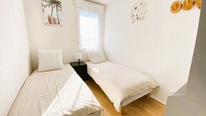 A small, clean room with two beds, a window with curtains, a small table with a lamp, and a wall decoration. - E03, welcoming 3* duplex near ocean & forest (Mimizan)