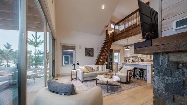 A spacious living area with a modern sofa, a stone fireplace, and a staircase leading to an upper level.