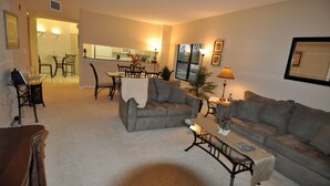 A living room with a grey sofa, a coffee table, and a dining area with chairs and a table. - Lake Front 3-bedroom condo walk to Nextera and beach in Juno Beach (JUNO BEACH)