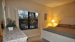 A bedroom with a large window, a bedside lamp, a bed with a headboard, and a small table with a plant. - Lake Front 3-bedroom condo walk to Nextera and beach in Juno Beach (JUNO BEACH)