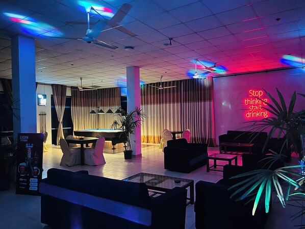Un espace de détente moderne avec une table de billard, des sièges confortables et un panneau lumineux au néon.