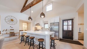 Una cocina amplia con una isla grande, taburetes de bar, lámparas colgantes y un refrigerador moderno.