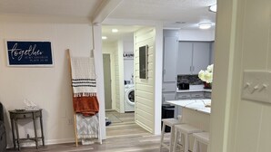 Een moderne keuken met witte kasten, een eethoek met witte krukken, en een wasruimte met een wasmachine.