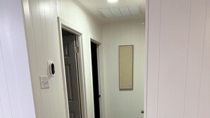 Een gang met houten vloer, witte wanden en een deur naar een andere kamer.