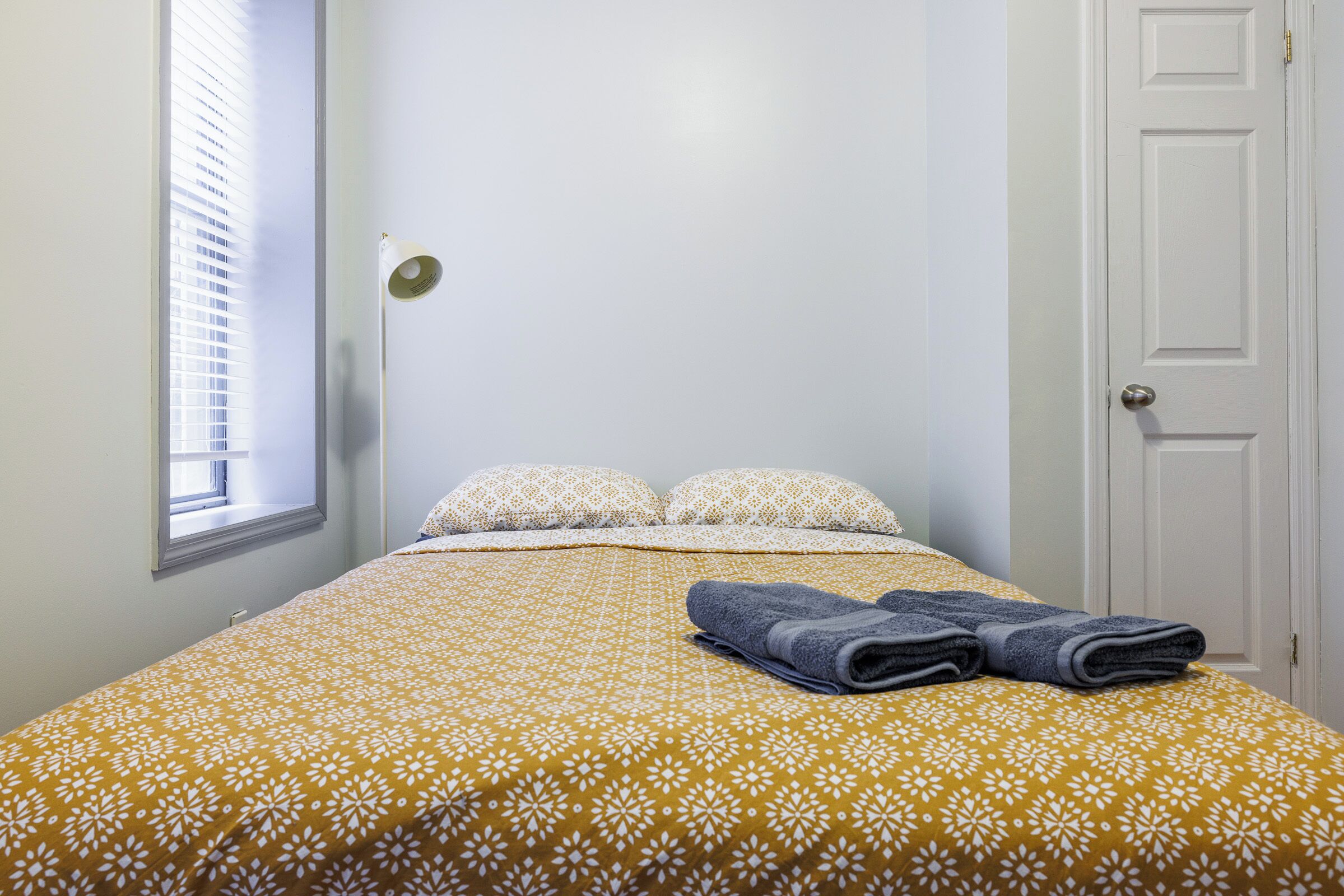 Un lit simple avec une couvre-lit à motifs, deux oreillers, une lampe de chevet et une porte.