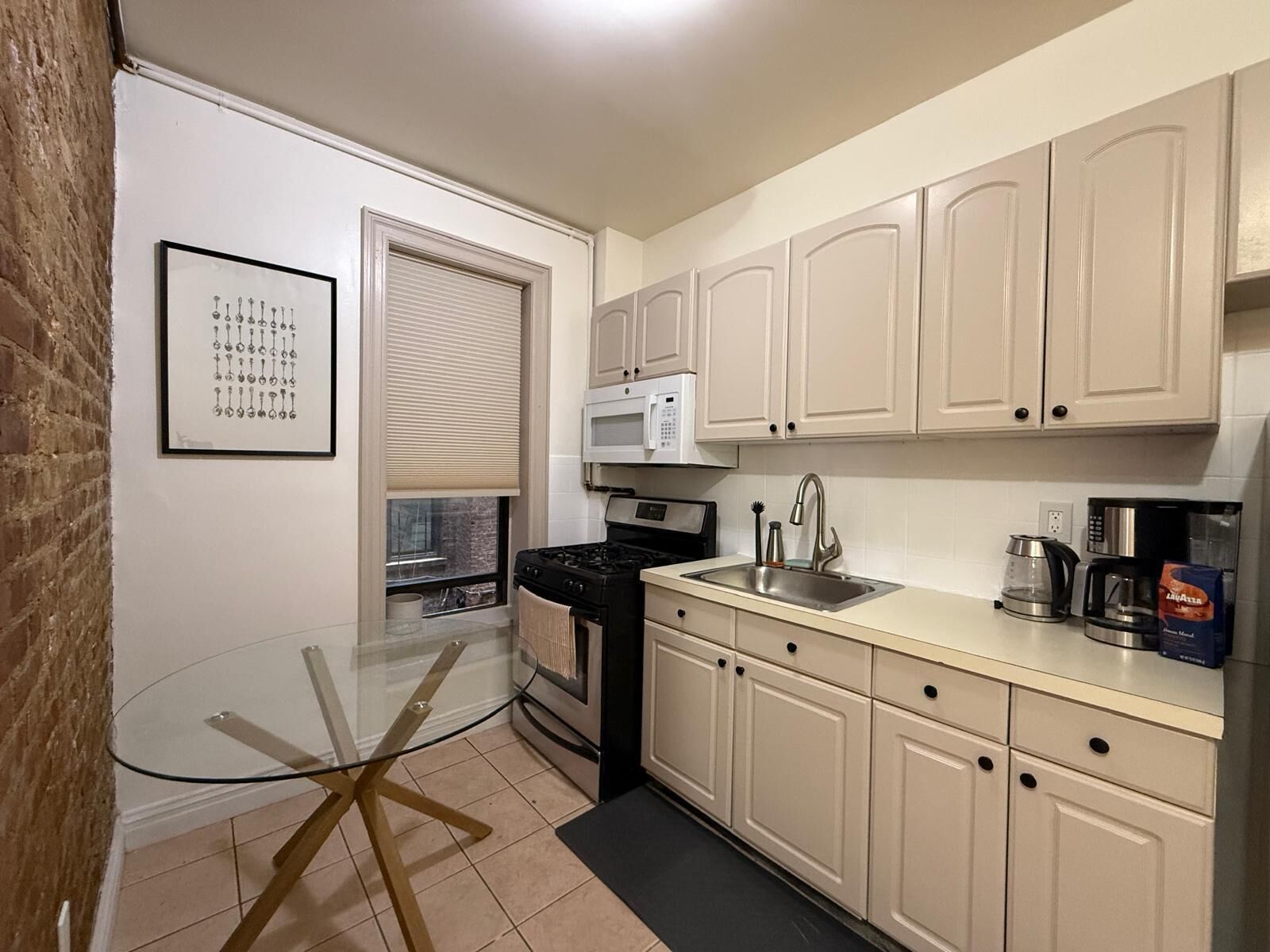 A compact kitchen with a glass table, a stove, a microwave, and cabinets.