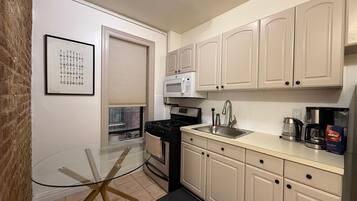 A compact kitchen with a glass table, a stove, a microwave, and cabinets.