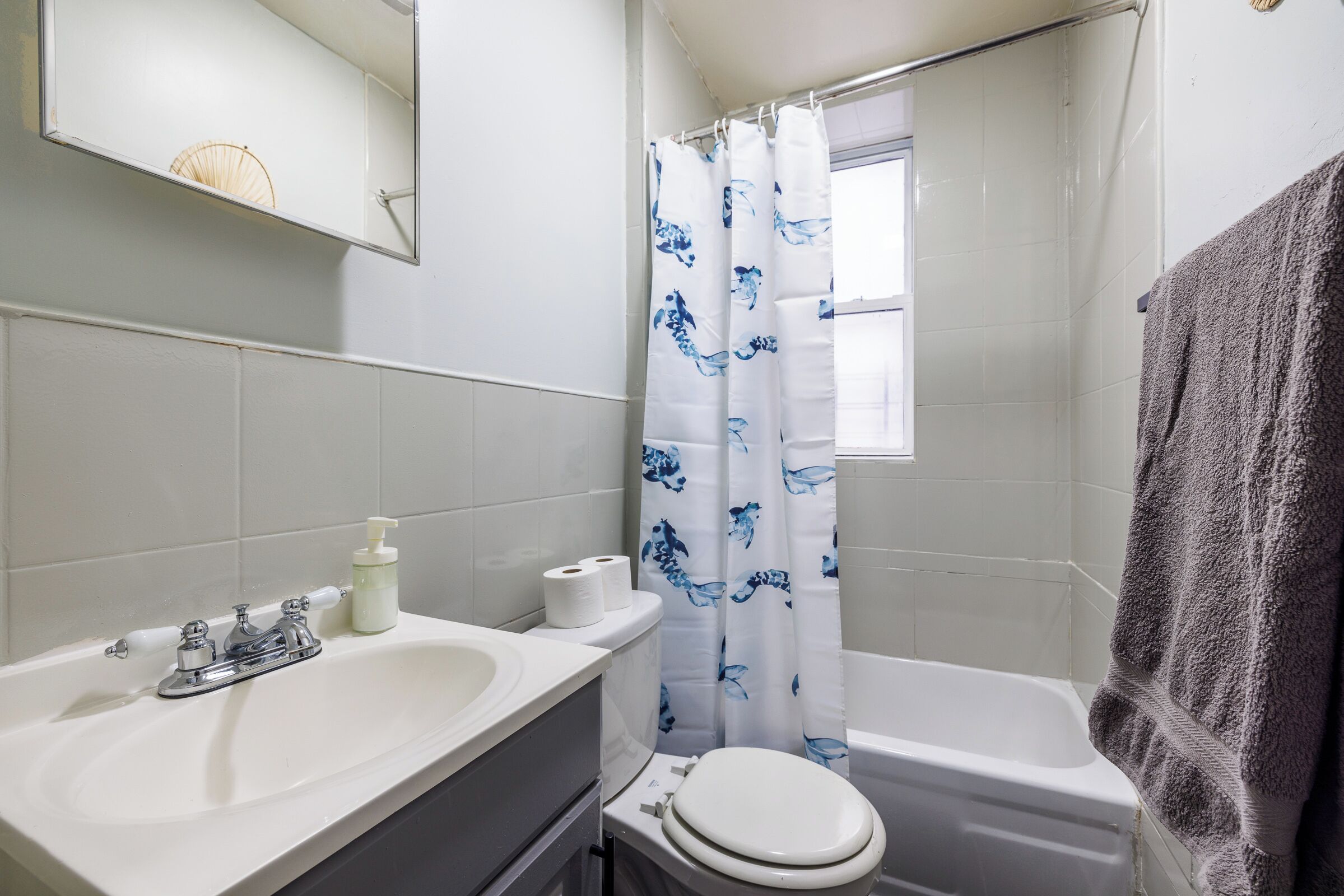 A bathroom with a white sink, toilet, and bathtub. There is a shower curtain with a blue pattern, and a towel is hanging on the wall.