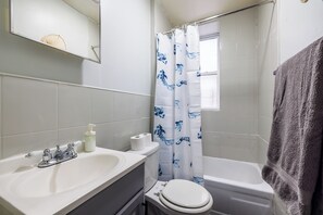 Ein Badezimmer mit einem weißen Waschbecken, einer Toilette und einer Badewanne. Ein blumiger blauer Vorhang ist über der Dusche, und ein Handtuch hängt an der Wand.