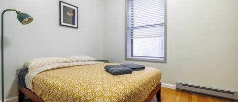 A bedroom with a bed, a window with blinds, a floor lamp, and a framed picture on the wall.