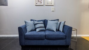 Ein blaues Sofa mit gestreiften Kissen, ein gerahmtes Pflanzenbild und ein Thermostat an der Wand.