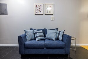 Ein blaues Sofa mit gestreiften Kissen, ein gerahmtes Pflanzenbild und ein Thermostat an der Wand.