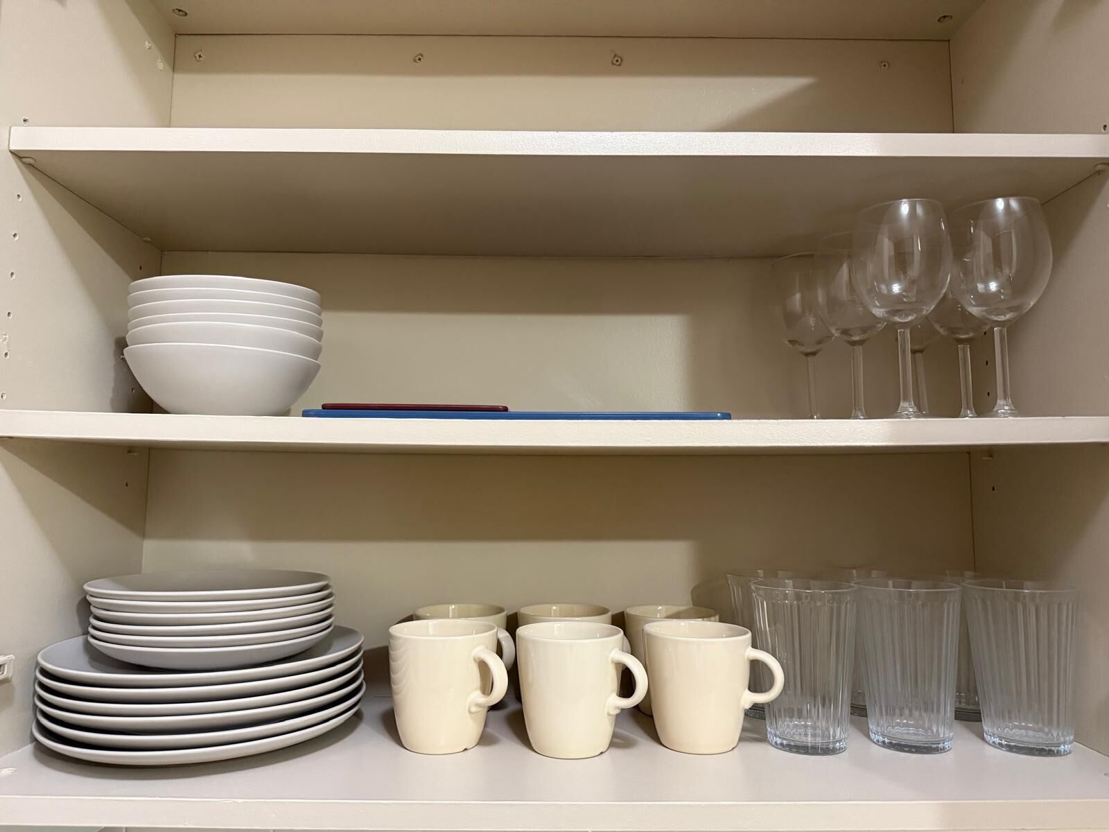 A shelf with stacked white bowls, a blue pen, and clear wine glasses.