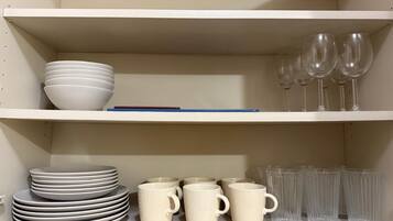 A shelf with stacked white bowls, a blue pen, and clear wine glasses.