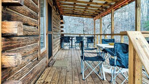 A log cabin with a wooden deck, outdoor seating, and a view of trees.