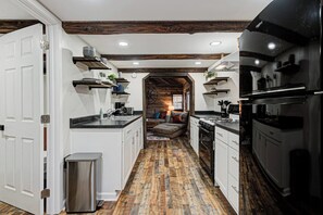 A narrow kitchen with white cabinets, a stainless steel refrigerator, and a wooden floor.