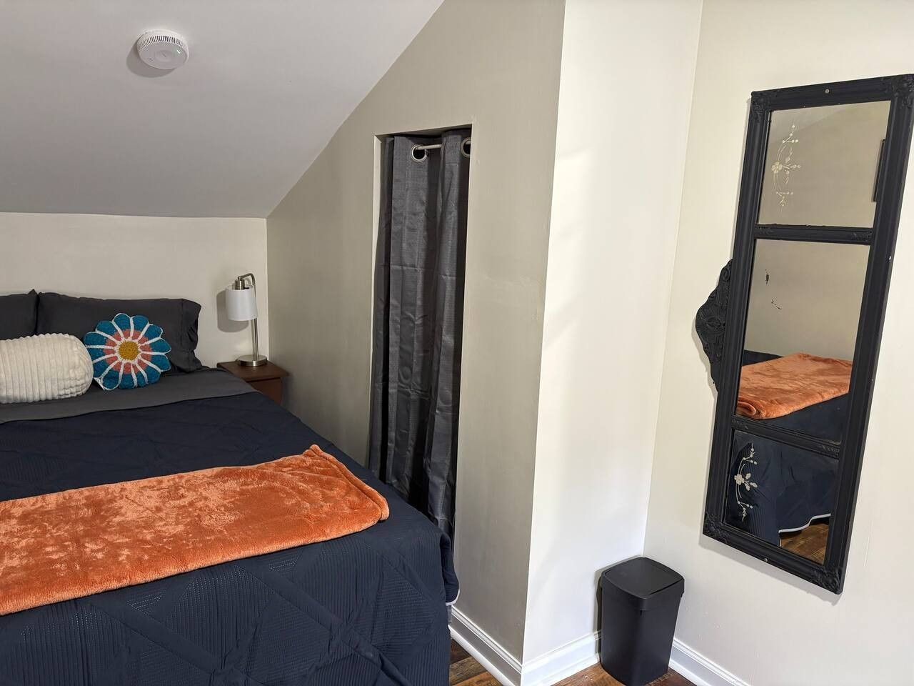 A bedroom with a bed, a nightstand, a mirror, a window with curtains, and a ceiling fan.