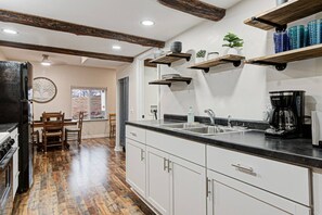 Una cocina con armarios blancos, encimera negra y vigas de madera en el techo.