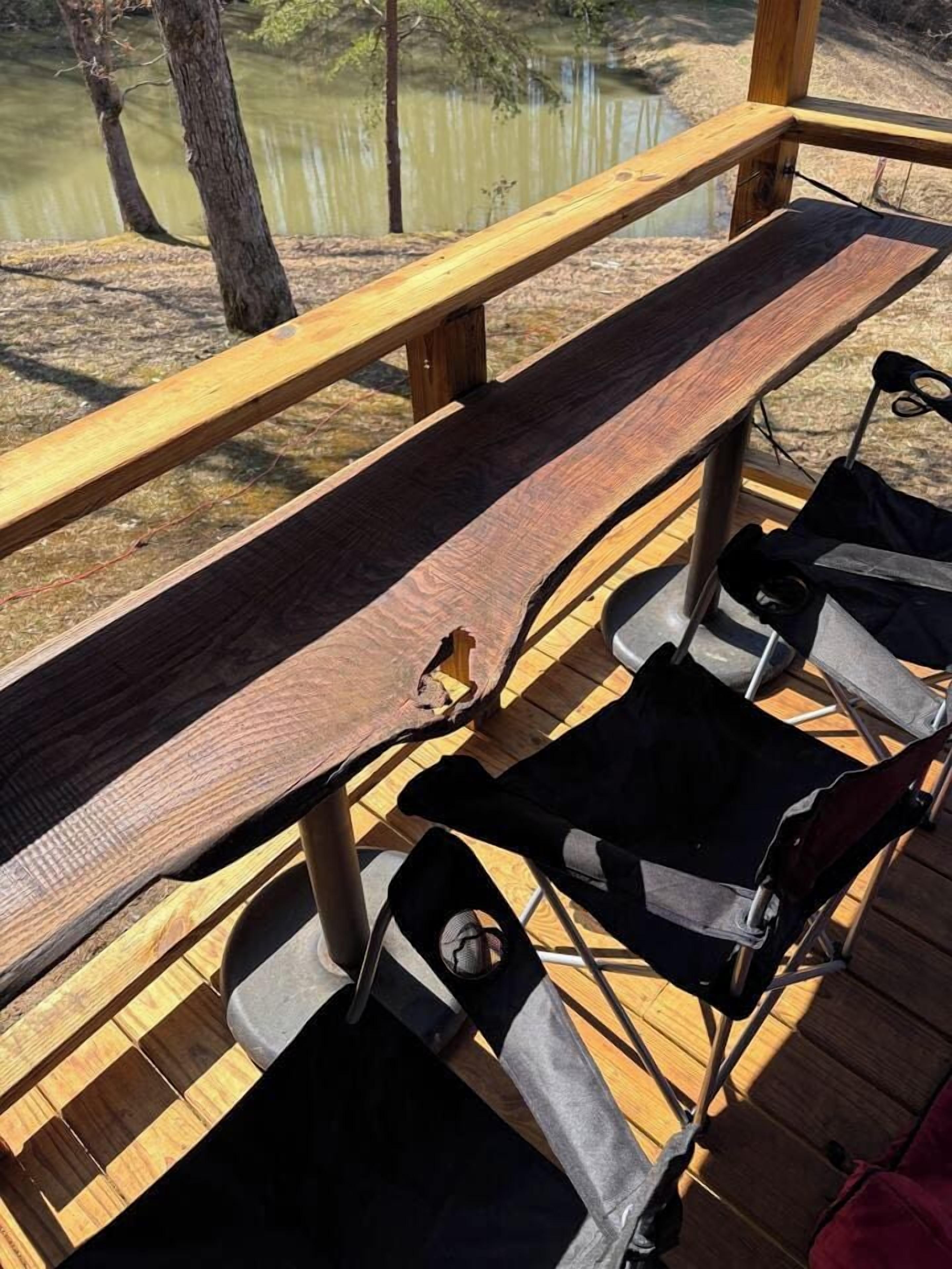 A wooden deck with a bench and two folding chairs.