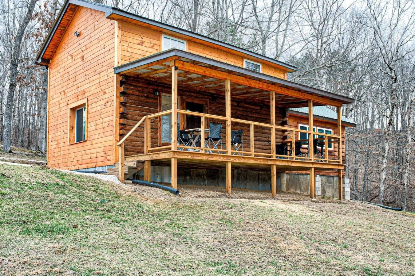 A wooden cabin with a covered porch and a small balcony, surrounded by trees.