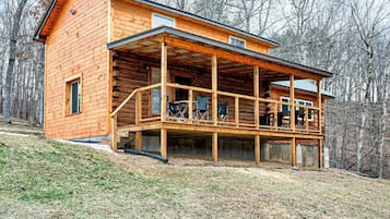 A wooden cabin with a covered porch and a small balcony, surrounded by trees.