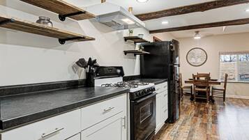 A kitchen with a gas stove, oven, black refrigerator, white cabinets, and a dining area with a table and chairs.