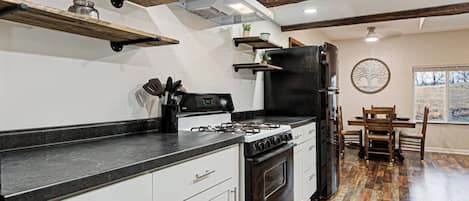 Une cuisine équipée d’une cuisinière à gaz, d’un four, d’un réfrigérateur noir, de meubles blancs et d’un coin repas avec une table et des chaises.
