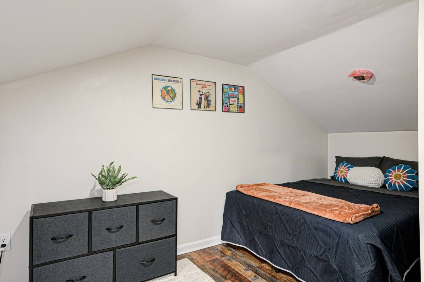 Une chambre à coucher avec un lit, une commode, une plante en pot et des œuvres d’art murales.