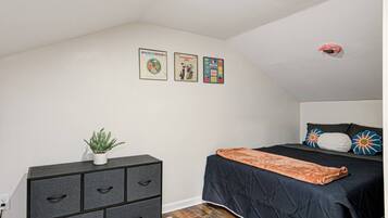Une chambre à coucher avec un lit, une commode, une plante en pot et des œuvres d’art murales.