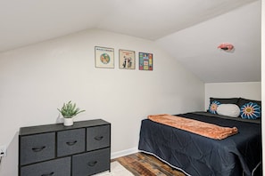 Ein Schlafzimmer mit einem Bett, einer Kommode, einer Topfpflanze und Wandbildern.