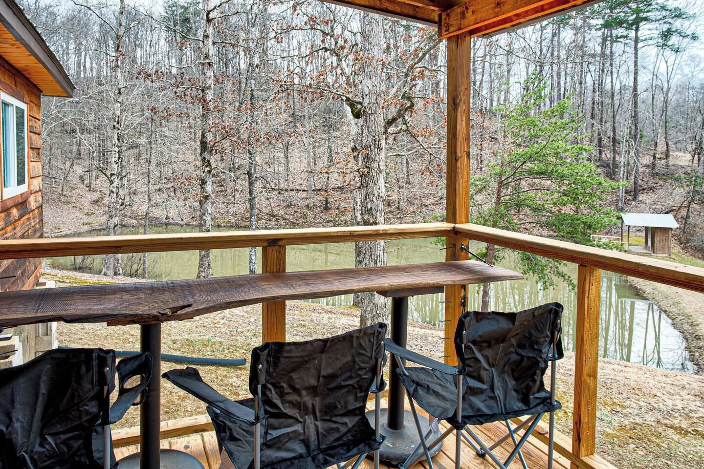 A wooden deck with a table and chairs overlooking a forested area and a body of water.