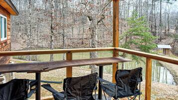 A wooden deck with a table and chairs overlooking a forested area and a body of water.