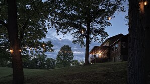 A rustic cabin with a deck, surrounded by trees and string lights.