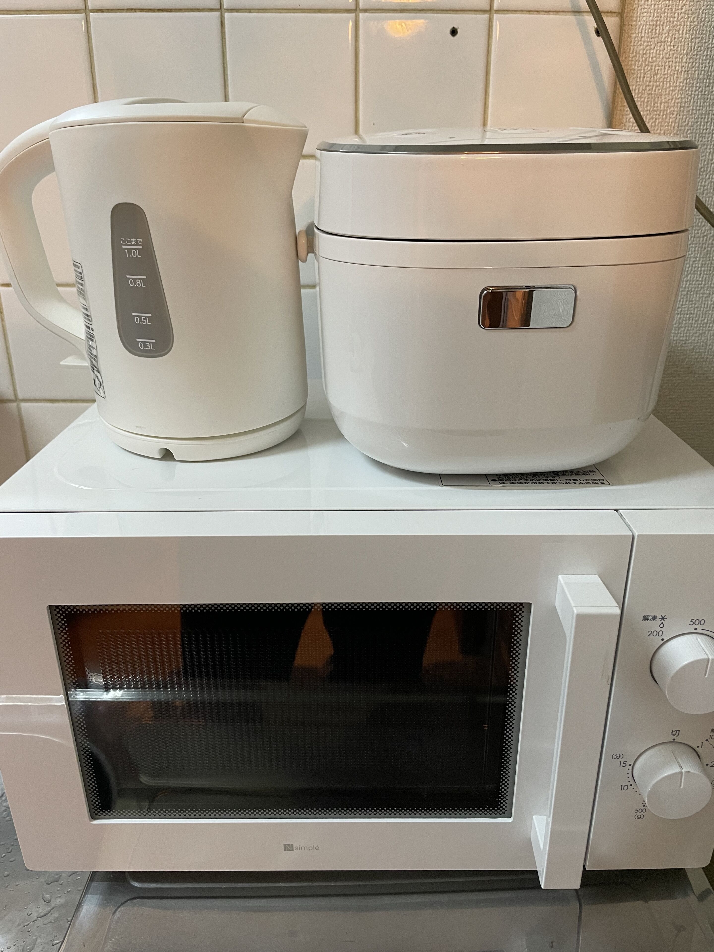 Un four à micro-ondes doté d’un écran numérique et d’un panneau de commande, une bouilloire électrique blanche et, au-dessus, une mijoteuse blanche.