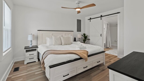 Une chambre à coucher comprenant un lit, des tables de chevet, un ventilateur de plafond, une armoire et une fenêtre.