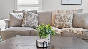 A living room with a beige sofa, patterned cushions, a wooden coffee table, and a potted plant.