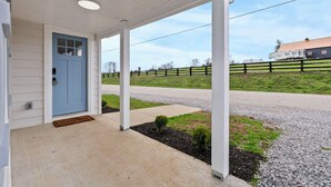 Un porche abrité avec une porte bleue, un chemin piétonnier en béton et une allée gravillonnée.