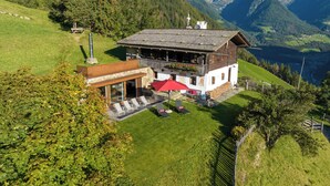 Een chalet met een houten balkon, een rode parasol en uitzicht op bergen.