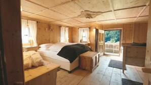 Een houten slaapkamer met een bed, een klein tafeltje en een raam met gordijnen.