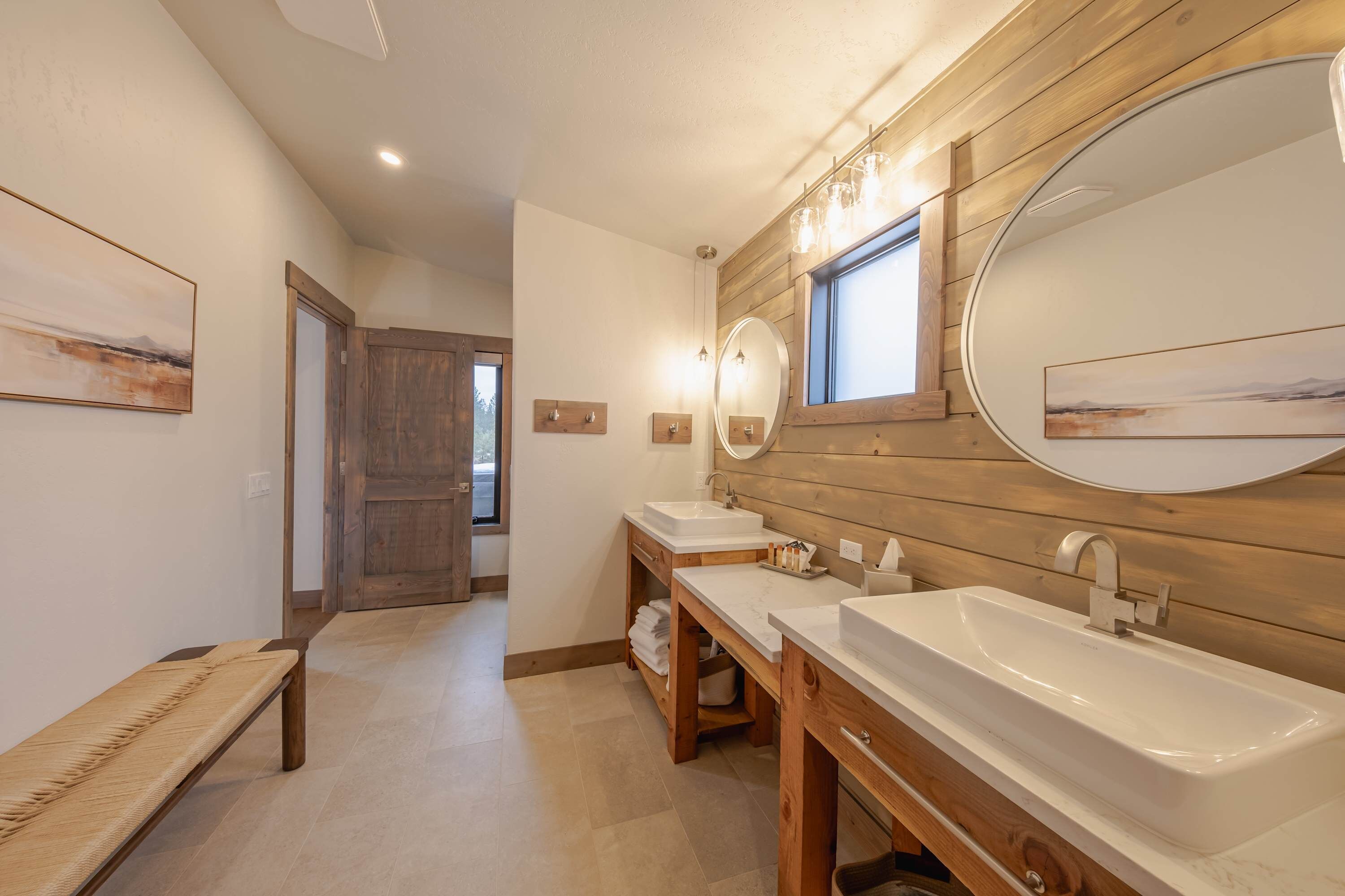Een badkamer met twee wastafels, een houten opbergmeubel en een bankje.